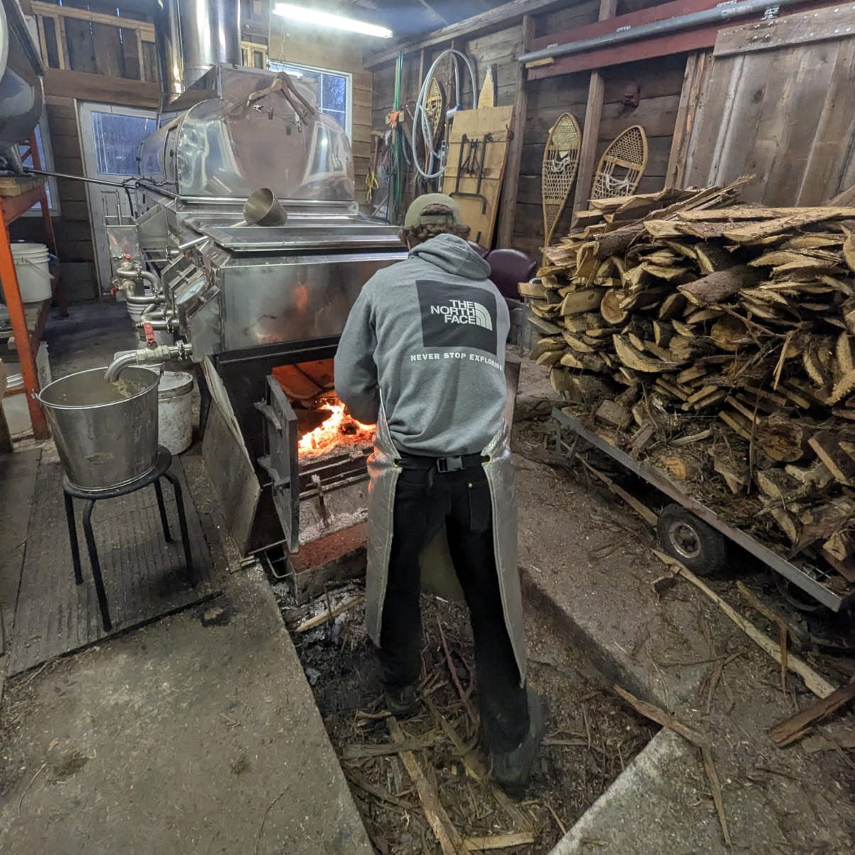 Person working with a large wooden evaporator in a sugar shack